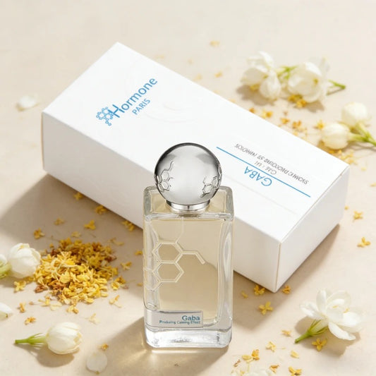 Product photograph of a Hormone Paris Gaba perfume bottle with a honeycomb design and its white box, presented on a light background with scattered white jasmine and yellow osmanthus flowers