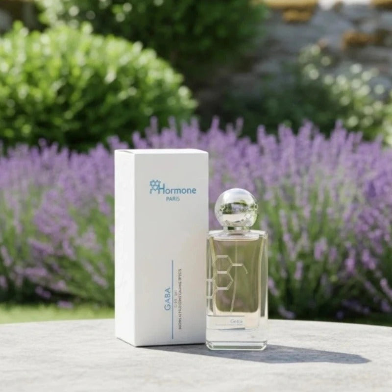 Hormone Paris Gaba perfume bottle and its white box with blue branding placed on a stone surface in a vibrant outdoor garden filled with purple lavender, the clear bottle featuring a subtle hexagonal pattern and a shiny spherical silver cap